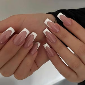 Puede incluir: Primer plano de una mano con uñas artificiales largas y cuadradas. Las uñas tienen un diseño de manicura francesa, con una base rosa nude y una punta blanca gruesa. Las uñas son brillantes y están bien cuidadas.
