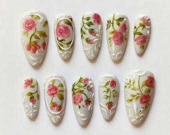 Può includere: Set di dieci unghie finte con base grigio chiaro, con rose rosa e foglie verdi dipinte a mano. Le unghie hanno una finitura lucida e sono decorate con volute bianche.