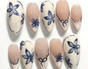 Peut inclure: Dix faux ongles ovales avec des motifs floraux. Les ongles ont une base crème. Chaque ongle présente un motif de fleur bleu peint à la main. Certains ongles ont une section nude et un nœud noir.