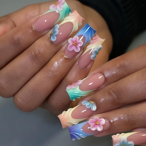 May include: Long, oval-shaped artificial nails with a French manicure design. Each nail features a gradient of colors, from pink to blue, and is adorned with 3D flower embellishments in pastel shades. Gold accents add a touch of elegance to the floral design.