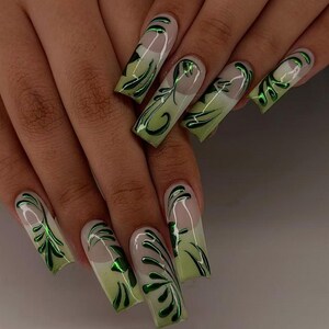 May include: Long, square-shaped acrylic nails with a light green gradient and a glossy finish. Each nail features a detailed, dark green, swirling design. The nails are shown on a hand with a light skin tone.