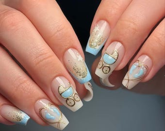 May include: Long, square acrylic nails with a baby shower design. The nails have a pale beige base, gold glitter, baby blue tips, and gold line art depicting baby carriages and footprints.