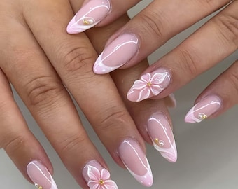Peut inclure: Ongles en amande avec une base rose clair et des pointes blanches. Les ongles sont décorés de fleurs roses en 3D, de perles et d'un motif tourbillonnant subtil. Manucure professionnelle.