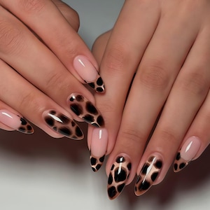 May include: A set of almond-shaped artificial nails with a nude base and a black and brown animal print design. The nails are long and well-manicured, showcasing a stylish and modern nail art look.