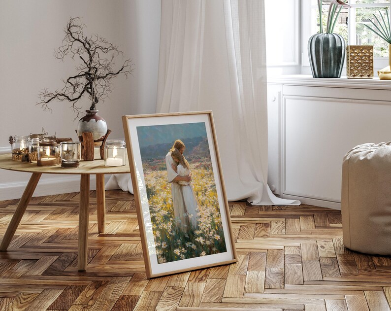 May include: A framed art print featuring a painting of two figures embracing in a field of flowers. The artwork is displayed in a light wood frame, leaning against a wall in a room with a wooden floor and a round wooden table.