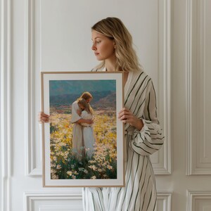 May include: A framed art print depicts two figures embracing in a field of white and yellow flowers, with a mountain range in the background. The artwork is in a wooden frame. The print has a warm color palette.