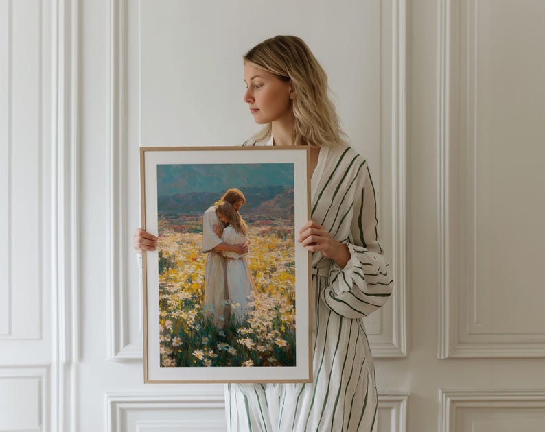 May include: A framed art print depicts two figures embracing in a field of white and yellow flowers, with a mountain range in the background. The artwork is in a wooden frame. The print has a warm color palette.