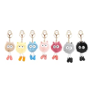 May include: Seven fuzzy pom-pom keychains in various colors including beige, yellow, blue, pink, magenta, gray, and black. Each keychain features two large white eyes, dangling white legs, and matching colored shoes attached to a gold metal ring.