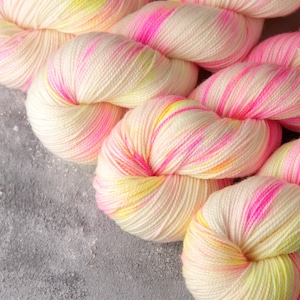 May include: Close-up of a skein of yarn with a white base and pink and yellow stripes. The yarn is soft and fluffy, and it is perfect for knitting or crocheting.