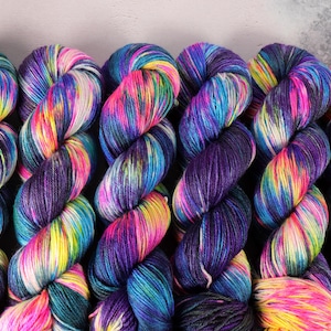 May include: A collection of colourful yarn skeins. The yarn displays a blend of bright hues, such as pink, yellow, blue, and purple. The yarn is twisted into neat bundles, ideal for knitting or crochet projects.