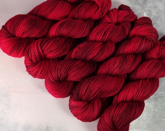 Può includere: Un primo piano di un gomitolo di lana rosso scuro. La lana è morbida e soffice, ed è perfetta per lavorare a maglia o all'uncinetto.
