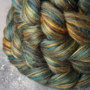 Könnte beinhalten: Nahaufnahme eines handgefärbten Garnknäuels. Das Garn ist eine Mischung aus teal, braunen und goldenen Farben, die ein strukturiertes, geflochtenes Aussehen erzeugt. Das Garn wird wahrscheinlich für Strick- oder Häkelprojekte verwendet.