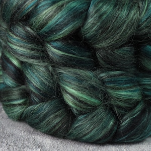 May include: Close-up of a braided fibre product in shades of green and black. The fibre appears soft and textured, with varying tones creating depth. The product is likely used for crafting or textile projects.