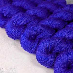 May include: Close-up of several skeins of vibrant blue yarn. The yarn is tightly wound, showing the texture of the fibres. The colour is a deep, saturated blue, creating a visually appealing display. Ideal for knitting and crochet projects.