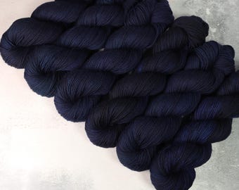 Puede incluir: Una colección de varias madejas de hilo azul marino oscuro dispuestas en un patrón diagonal. Cada madeja presenta una construcción de hebras fuertemente retorcidas con un brillo sutil, mostrando un color profundo y uniforme en toda la fibra.