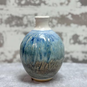 May include: A small, round ceramic vase with a blue and white glaze. The vase has a textured surface and a slightly flared lip.