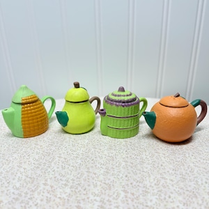 May include: Four miniature ceramic teapots in a row. The teapots are painted in bright colors, including green, yellow, orange, and purple. Each teapot has a unique design, such as a beehive pattern or a striped pattern. The teapots have small handles and spouts.