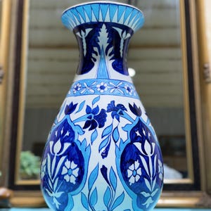 May include: A ceramic vase with a white base and intricate blue floral patterns. The vase features a flared top and a bulbous body, with detailed designs of flowers and leaves. The color palette includes shades of light and dark blue.