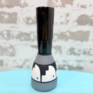 May include: A hand-painted ceramic vase with a black top and a gray base. The vase features a unique design with white and black shapes and teal accents. The vase is approximately 8 inches tall.