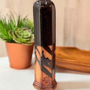 May include: A tall, ceramic incense holder with a dark brown glaze and a lighter brown, textured design. The holder has a hexagonal base and a loop at the top. The design is reminiscent of a pillar.