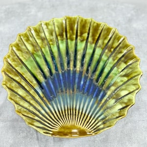 May include: A decorative ceramic dish with a scalloped edge. The dish features a fan-like design with shades of green, blue, and brown. The dish has a glossy finish and is likely used for serving or display.