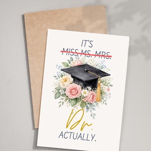 May include: A graduation card featuring a black mortarboard with a gold tassel, set against a backdrop of pink and white flowers. The card's text reads "It's Dr. Actually", with "Miss, Ms., Mrs." crossed out.