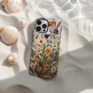 May include: A floral phone case featuring a watercolor design of colorful flowers in shades of orange, purple, pink, and yellow. The case is set on a bed of white sand with seashells scattered around it.