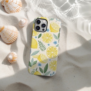 Könnte beinhalten: Eine Handyhülle mit Zitronenmuster. Die Hülle hat einen cremefarbenen Hintergrund mit Illustrationen von gelben Zitronen, grünen Blättern und kleinen blauen Blumen. Die Hülle liegt auf einer sandigen Oberfläche mit Muscheln.