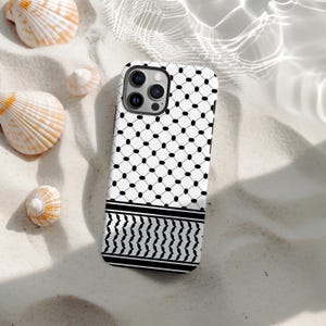 May include: A white and black patterned phone case with a geometric design. The case features a repeating pattern of black dots and lines, with a black and white border at the bottom. The case is surrounded by seashells on a sandy surface.