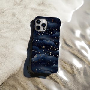 Pode incluir: Capa de telefone azul escuro com um design celestial de estrelas douradas, luas crescentes e formas de nuvens. A capa tem um acabamento brilhante e est&aacute; sobre uma superf&iacute;cie arenosa.