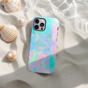 May include: A smartphone case with a colorful, iridescent design in shades of blue, pink, and green. The case is lying on a bed of white sand, with seashells scattered around it. The case has a black border and a camera module.
