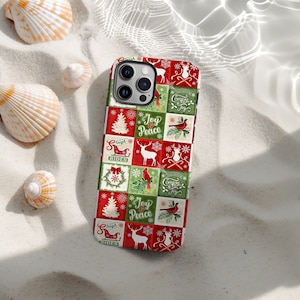 Può includere: Una custodia per smartphone con un design natalizio festivo. La custodia presenta un motivo patchwork di quadrati rossi e verdi con immagini natalizie come renne, alberi di Natale e le parole "Joy Peace" e "Comfort Joy".