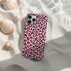 May include: A pink and black leopard print phone case. The case is on white sand, with seashells nearby. The case has a glossy finish and a camera cutout. The background has a water effect.