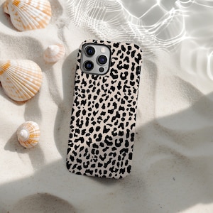 Peut inclure: Coque de smartphone avec un motif léopard noir sur fond beige. L'étui est posé sur du sable, entouré de coquillages.