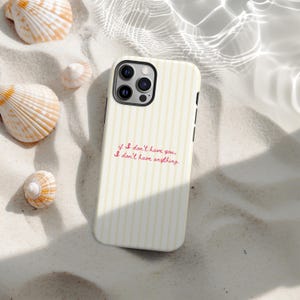 Puede incluir: Una funda de teléfono crema con rayas verticales amarillas y el texto "if I don't have you, I don't have anything" en escritura rosa. La funda está rodeada de conchas marinas sobre una superficie arenosa.