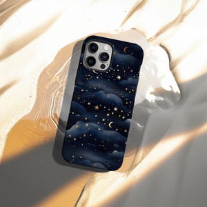 Pode incluir: Capa de telefone azul escuro com um design celestial. Apresenta estrelas douradas, luas crescentes e formas de nuvens. A capa tem um acabamento brilhante e um recorte para a c&acirc;mera.