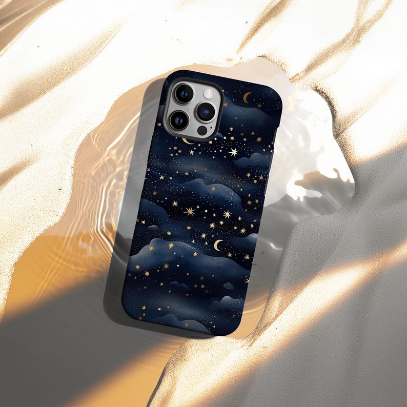 Pode incluir: Capa de telefone azul escuro com um design celestial. Apresenta estrelas douradas, luas crescentes e formas de nuvens. A capa tem um acabamento brilhante e um recorte para a c&acirc;mera.