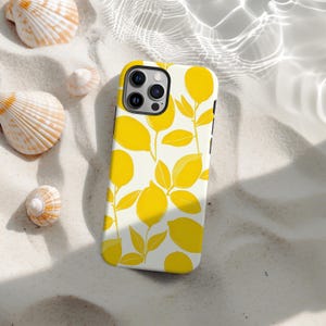 Könnte beinhalten: Weißes iPhone-Case mit gelbem Zitronen- und Blättermuster. Auf Sand mit Muscheln platziert, zeigt das Design stilisierte gelbe Zitronen und Blätter auf weißem Hintergrund, was eine sommerliche Ästhetik erzeugt.