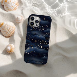 Op de afbeelding: Een smartphonehoesje met een donkerblauw nachthemelontwerp met gouden sterren, manen en wolken. De hoes ligt op wit zand met verspreide schelpen.