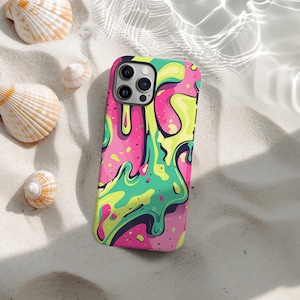 Puede incluir: Una funda de teléfono colorida con un diseño abstracto vibrante. La funda presenta una base rosa con formas verdes, amarillas y azul oscuro fluidas. La funda del teléfono está sobre arena blanca, con conchas marinas esparcidas.