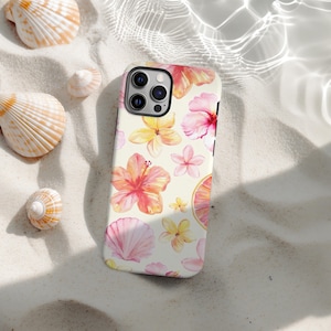 May include: A smartphone case with a floral design featuring hibiscus and other flowers in shades of pink, yellow, and orange. The case also includes a seashell and a slice of citrus fruit. The case is on a sandy surface with seashells.