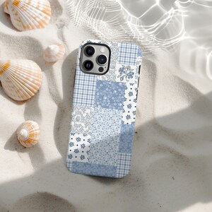 Puede incluir: Funda de teléfono con diseño de patchwork azul y blanco con varios estampados florales y de cuadros. La funda está sobre una superficie arenosa con conchas marinas. Accesorio para teléfono móvil.