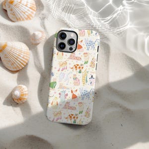 May include: A white iPhone case with a repeating pattern of illustrated cats in different outfits and poses. The cats are in various colours and patterns. The case is surrounded by seashells on a sandy surface.