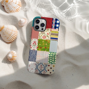 以下が含まれることがあります： ギンガムチェック、花柄、水玉模様など、さまざまなパターンが施されたカラフルなパッチワークの携帯電話ケース。砂浜の表面に貝殻が置かれ、ビーチのような雰囲気を作り出しています。