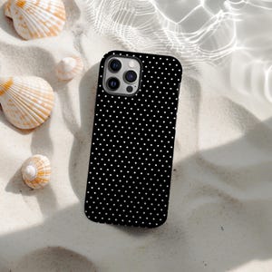 May include: A black phone case with a white polka dot design lies on sand, with seashells scattered around. The case features a multi-lens camera module.