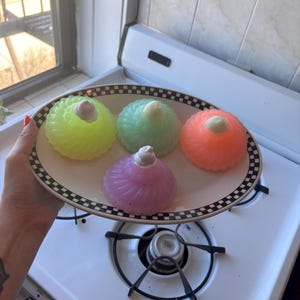 May include: Four colorful gelatin desserts on a black and white checkered plate. The desserts are green, pink, orange, and purple. Each dessert has a white swirl on top.