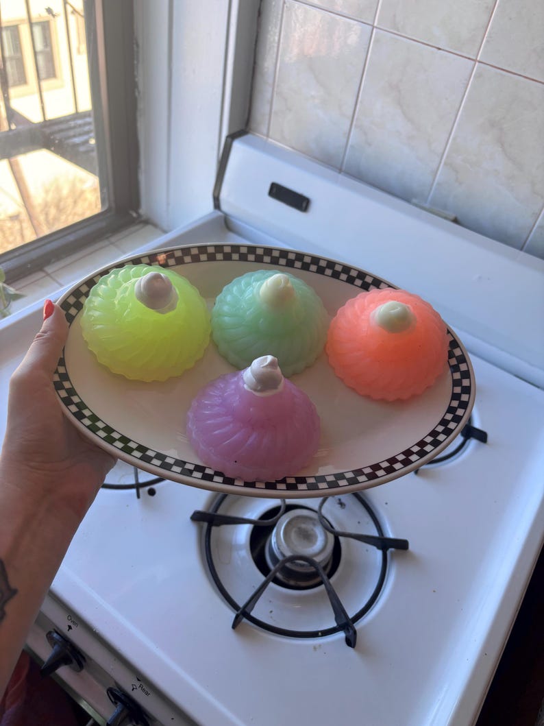 May include: Four colorful gelatin desserts on a black and white checkered plate. The desserts are green, pink, orange, and purple. Each dessert has a white swirl on top.