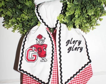May include: A white fabric hair scarf with black rickrack trim and red and white gingham backing. One side features an embroidered bulldog wearing a red sweater and cap with a letter G, while the other side displays the embroidered text glory glory.