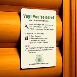 Puede incluir: Un letrero rectangular blanco con texto verde y un icono de llave, que proporciona instrucciones sobre cómo desbloquear una puerta. El letrero está montado sobre una superficie de madera. El texto incluye "Yay! You're here!" y "www.loggedoutrentals.com".