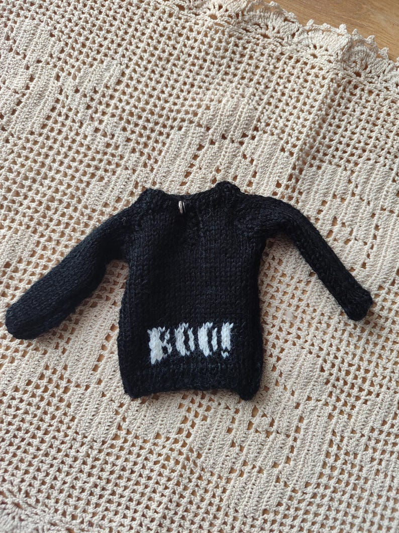 May include: Black knitted sweater with long sleeves and a white "BOO!" design on the front.